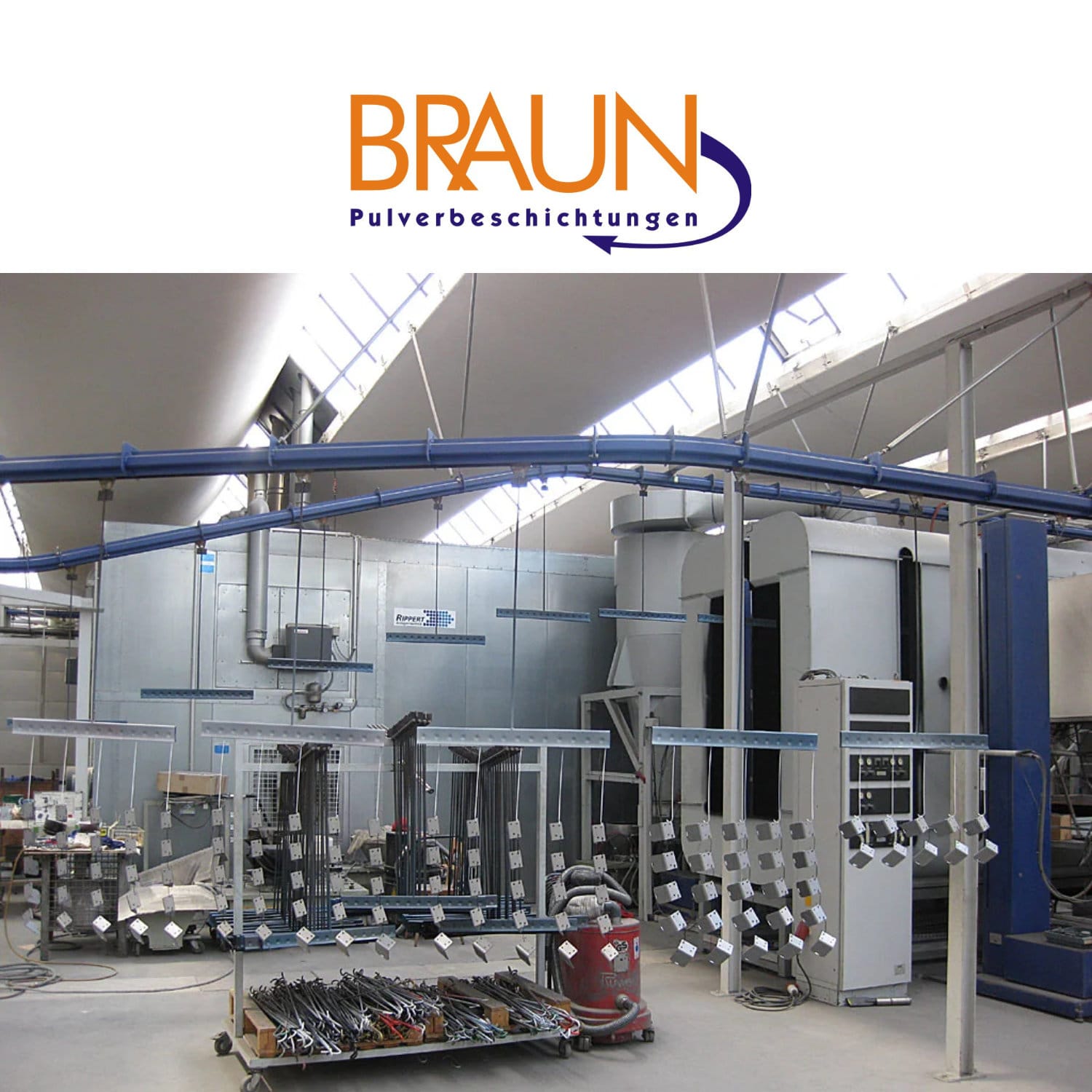 Das Bild zeigt eine hochmoderne Pulverbeschichtungsanlage in einem lichtdurchfluteten Industriebetrieb. Metallteile verschiedenster Größen hängen an einer automatisierten Hängebahn und werden für die Pulverbeschichtung vorbereitet. Diese fortschrittliche Technik ermöglicht eine gleichmäßige, effiziente und umweltfreundliche Oberflächenveredelung – ideal für Serienfertigung und industrielle Anwendungen.